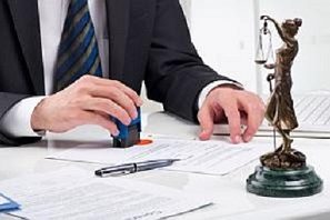 Neue Urkunden Ein Anwalt stempelt Dokumente neben einer Justitia-Statue auf einem Tisch.