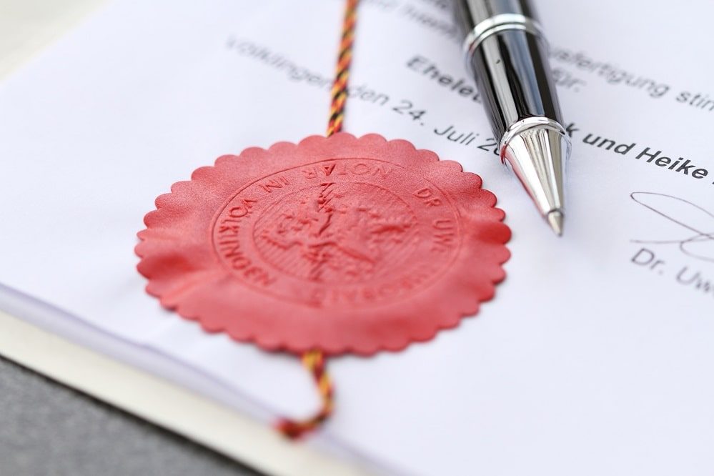 Beglaubigung Apostille Rotes Wachssiegel mit Schriftzug, daneben ein Kugelschreiber auf Papier. Dokumentenbeglaubigung.
